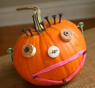 An artistic pumpkin design featuring rubber bands forming a mouth, a button serving as a nose, and screws representing the eyes, creatively assembled to represent a whimsical character.